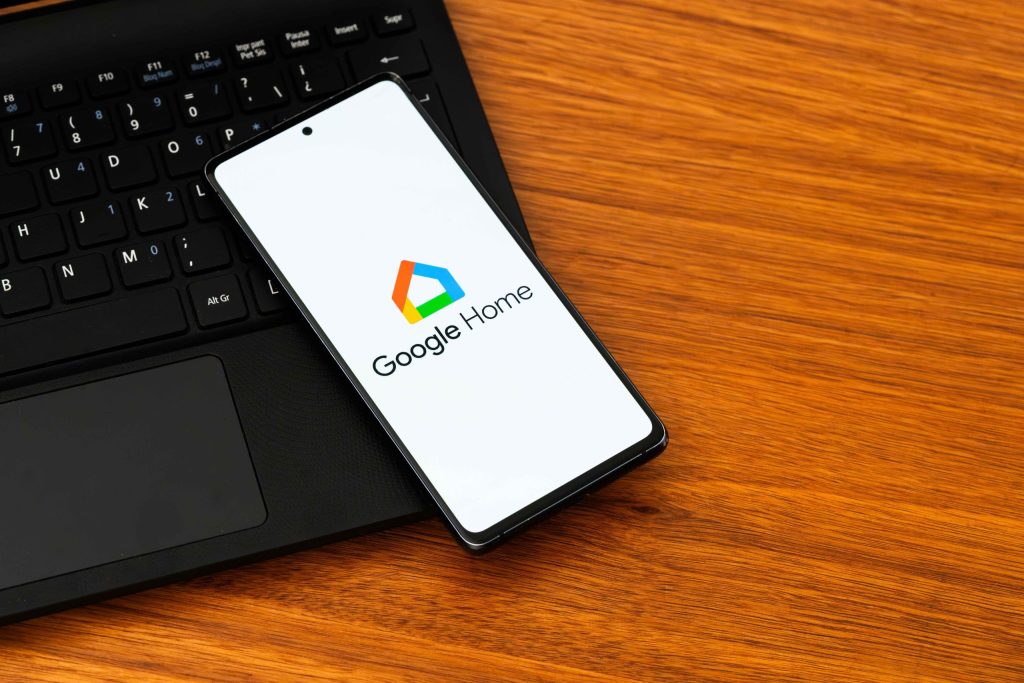 Smartphone displaying the Google Home logo on a wooden desk next to a laptop keyboard