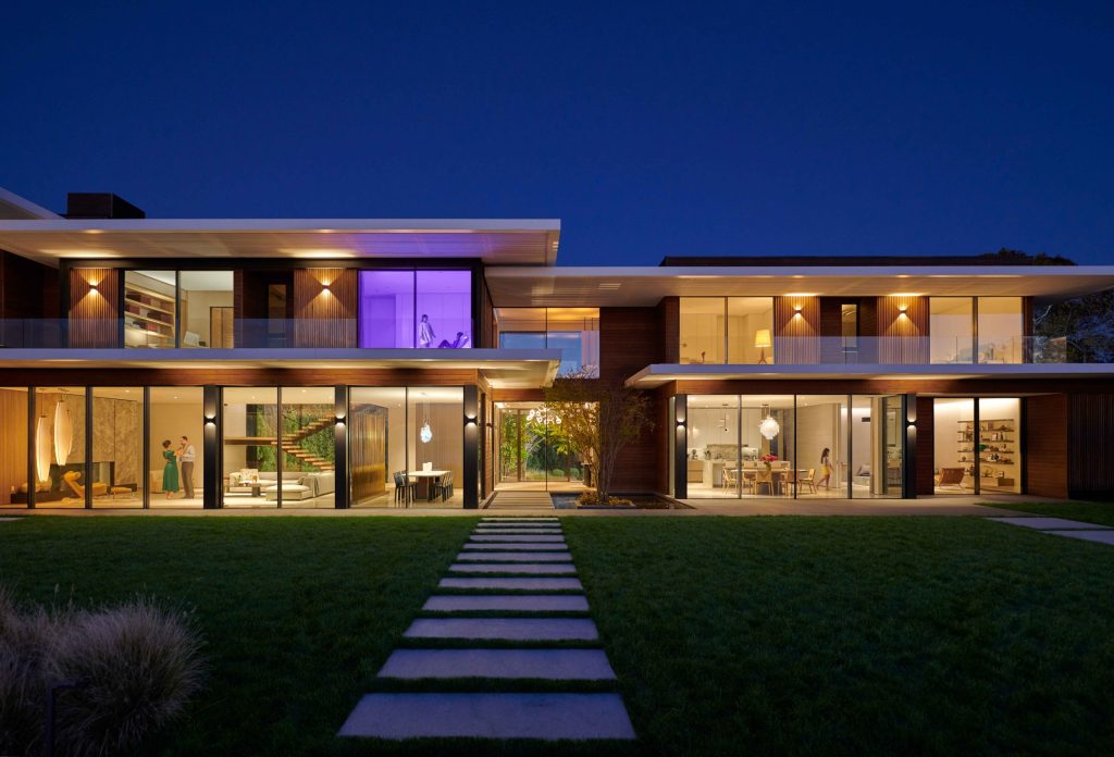 Modern luxury home at dusk with warm interior lighting and large glass façade