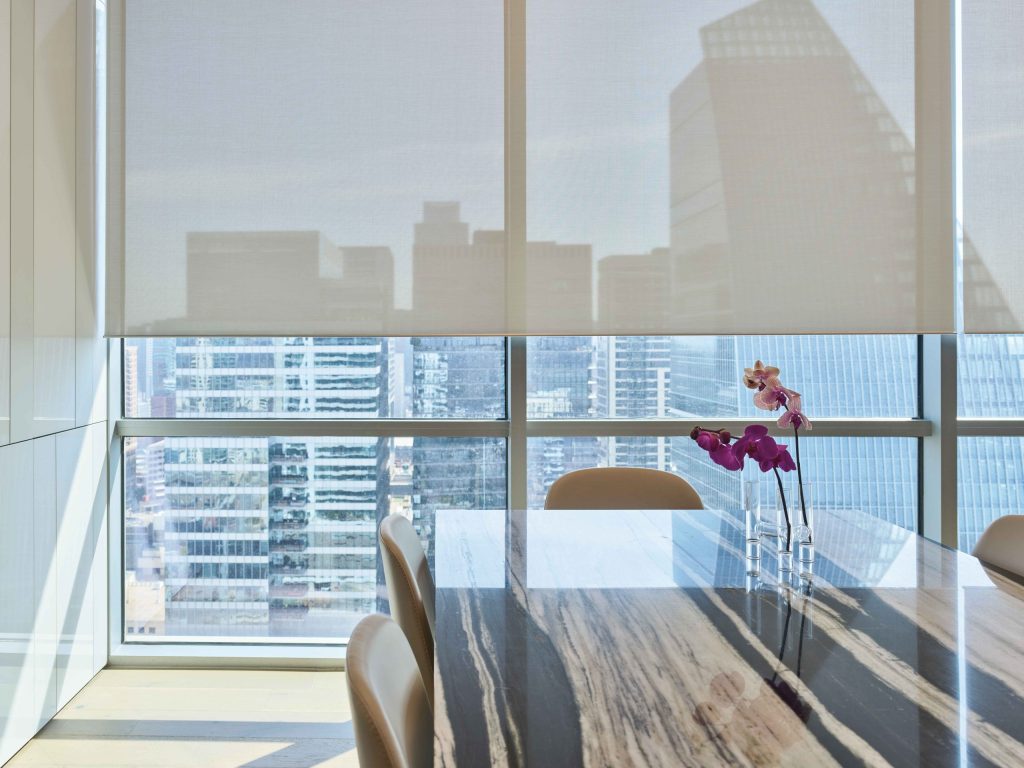 Dining room with lowered shades filtering daylight across a stone table