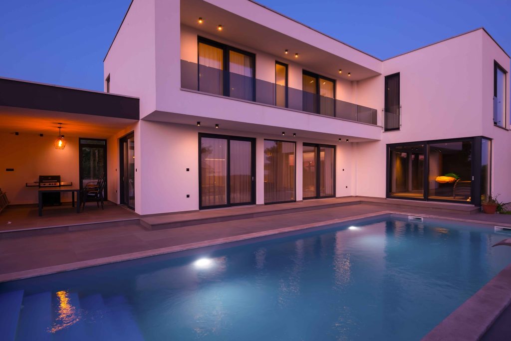 Modern luxury house at dusk with pool and warm interior lighting
