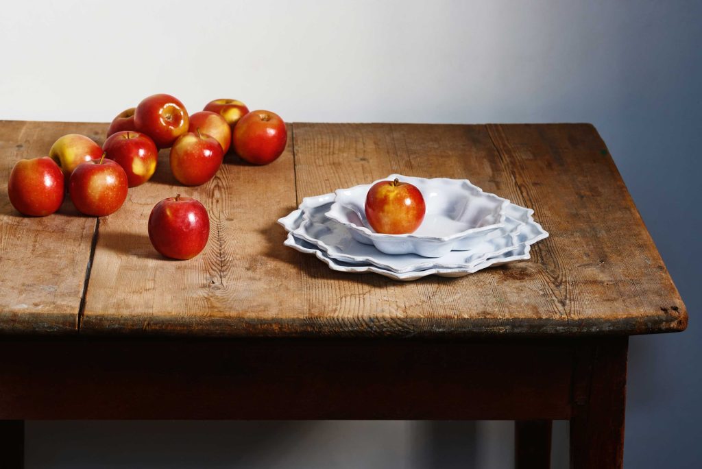Astier de Villatteの白い陶器と赤いリンゴを木製テーブルに配したビジュアル