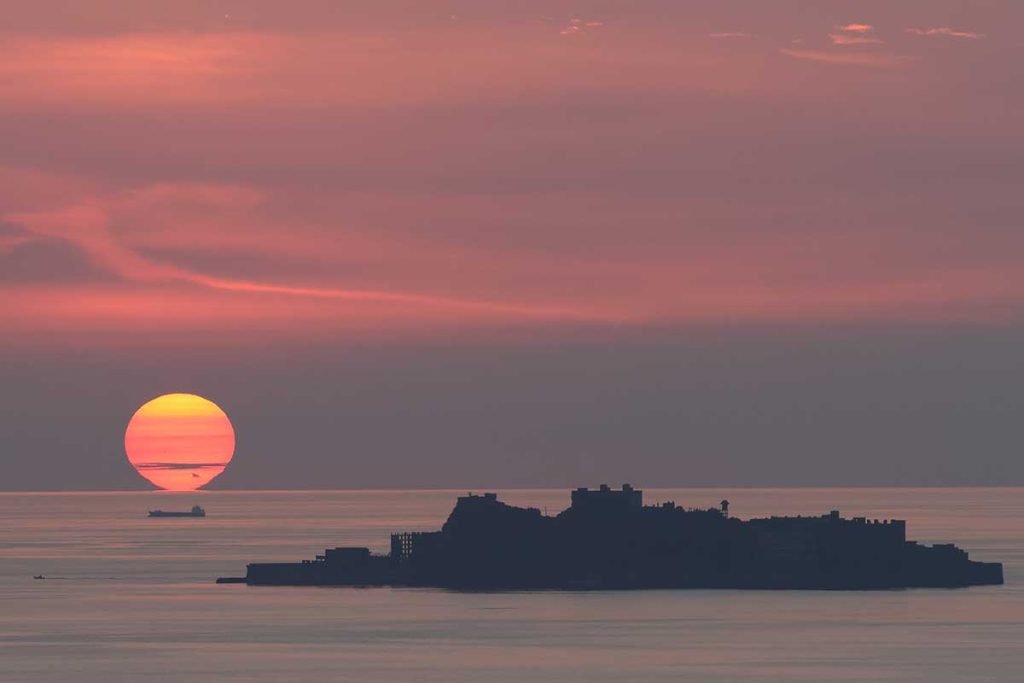 水平線に沈む大きな夕陽と長崎・軍艦島を捉えた山口政勝の写真