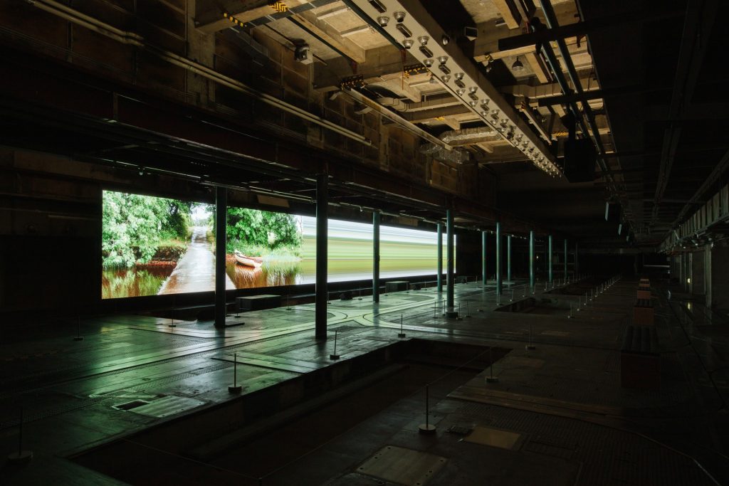 旧印刷工場跡の長い展示空間に水辺と樹木の映像が連続して映し出される《async - immersion》
