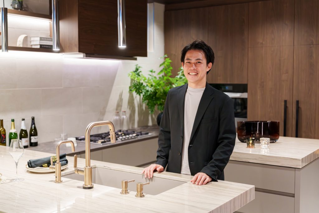 天然石のキッチンカウンターの前に立つ男性と、木製キャビネットを備えたキッチン