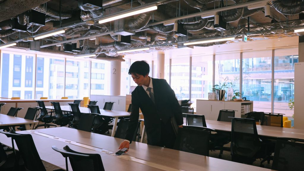 Office worker tapping a smartphone on an NFC tag at a desk to access personalized lighting and airflow controls