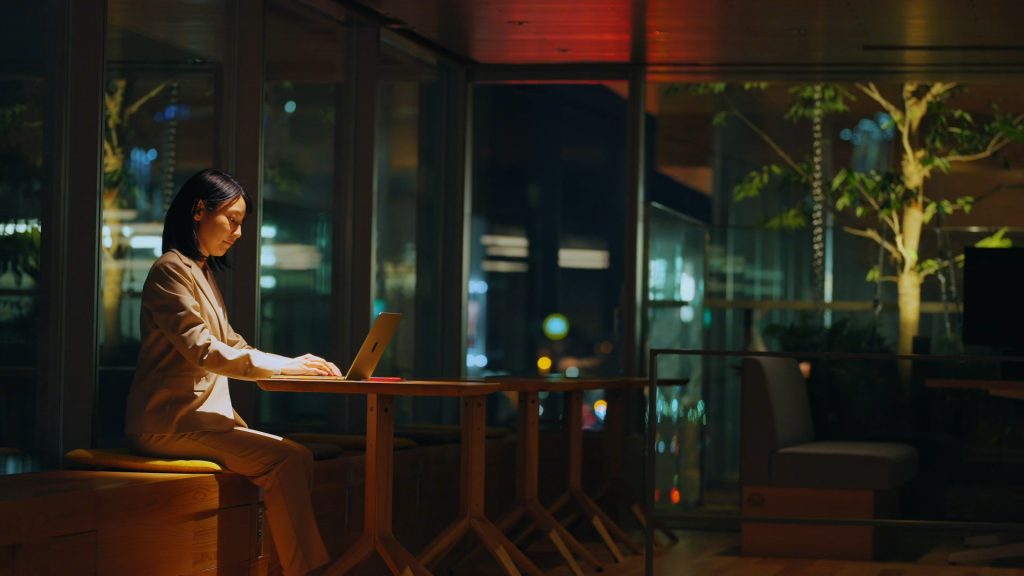 Office worker using a laptop in an illuminated workspace overlooking Tokyo at night