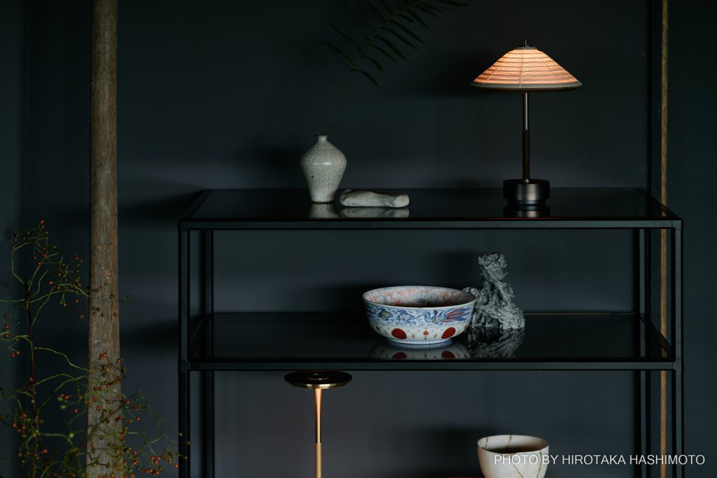 Teseraの黒いシェルフに置かれたAmbientecのポータブル照明と古い器。小さな灯りが陰影を生み出す